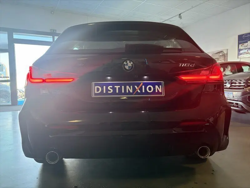 Vue arrière d'une BMW Série 1 noire métal 118d 150ch avec feux LED allumés dans un showroom.