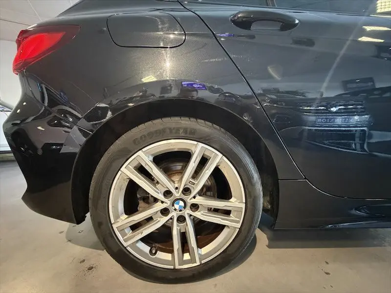 Gros plan sur la roue arrière droite d'une BMW Série 1 noire métal avec jante alliage cinq branches en intérieur.