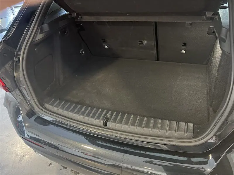 Coffre ouvert vu de l'arrière d'une BMW Série 1 noire métal, montrant un espace de chargement propre et vide.