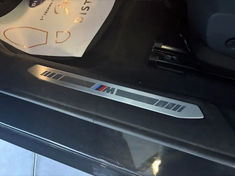 Gros plan sur la plaque de seuil de porte BMW M en métal brossé, intérieur noir d'une Série 1 F40 noire métallisée.