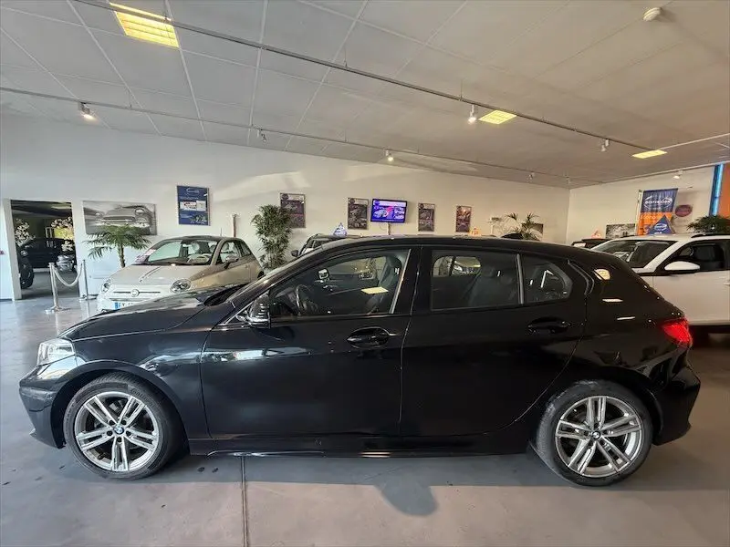BMW Série 1 noire métal vue de profil côté gauche en intérieur, avec jantes alliage et lignes sportives M Sport.