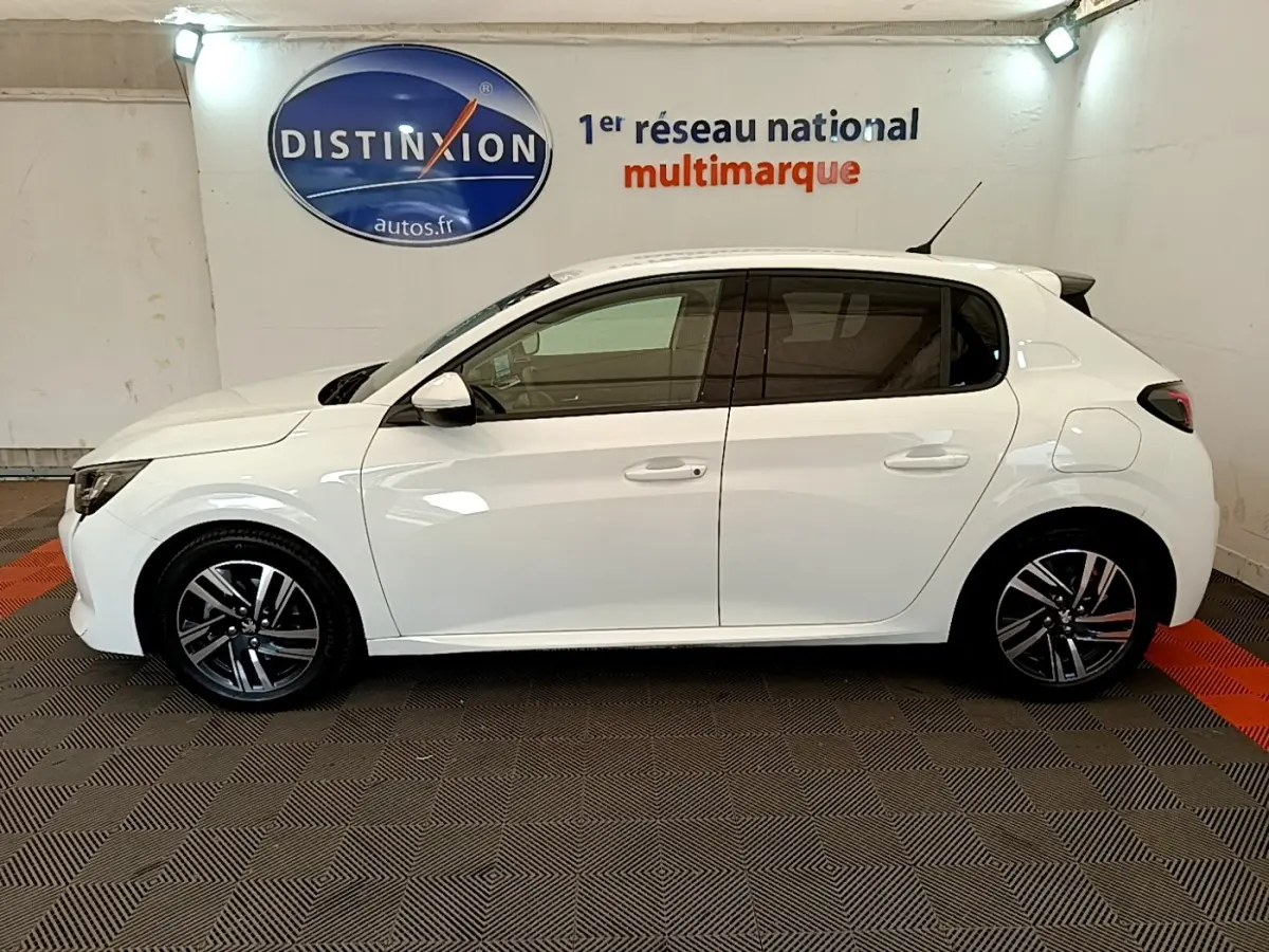 Profil droit d'une Peugeot 208 blanche 2021 PureTech 100 S&S Allure Business en intérieur avec jantes alliage noires et grises.