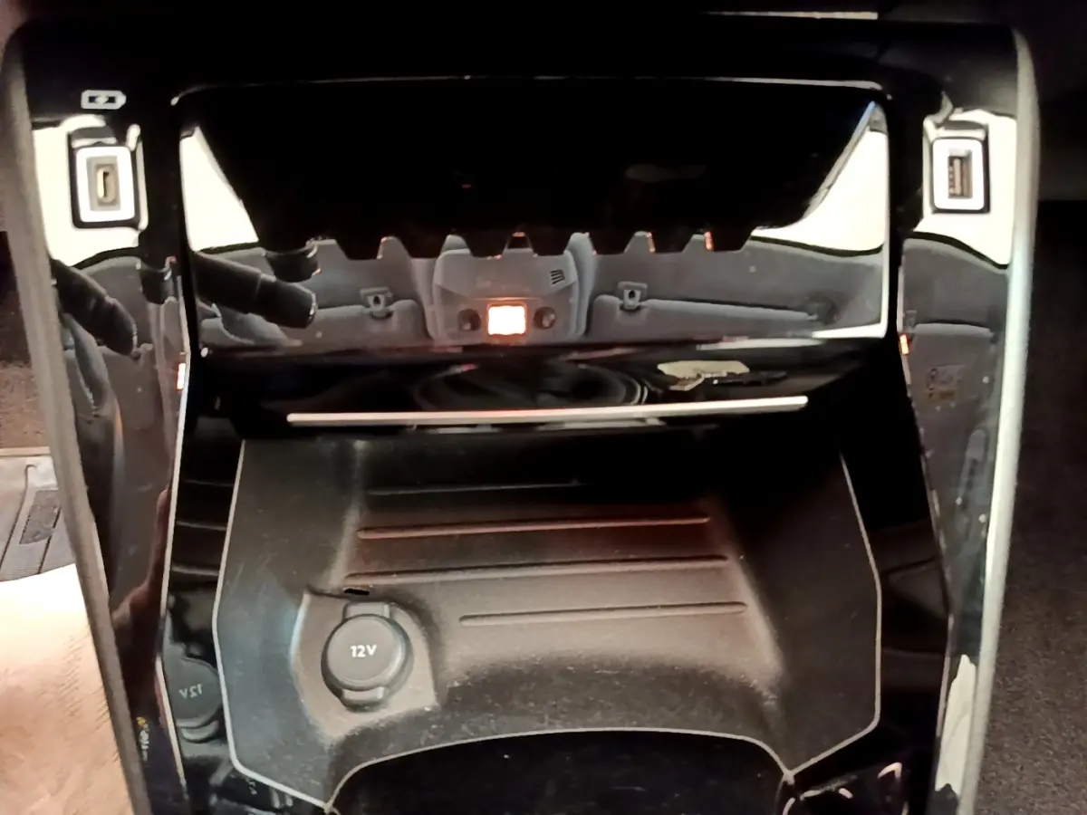 Gros plan sur la console centrale noire du Peugeot 208 PureTech 100, avec prise 12V visible au centre.