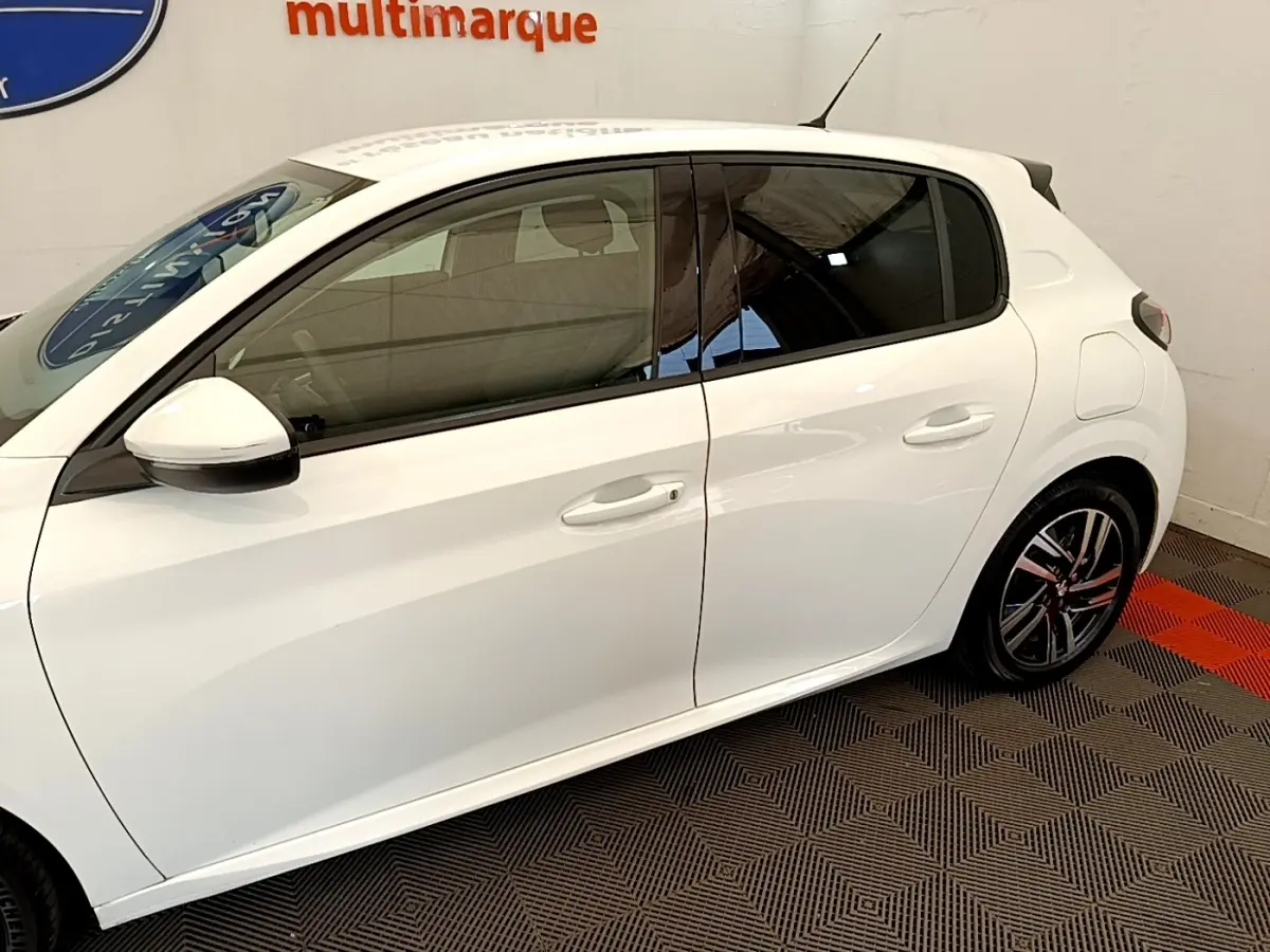 Vue de profil côté gauche d'une Peugeot 208 blanche PureTech 100 S&S Allure Business avec jantes alliage et vitres teintées.