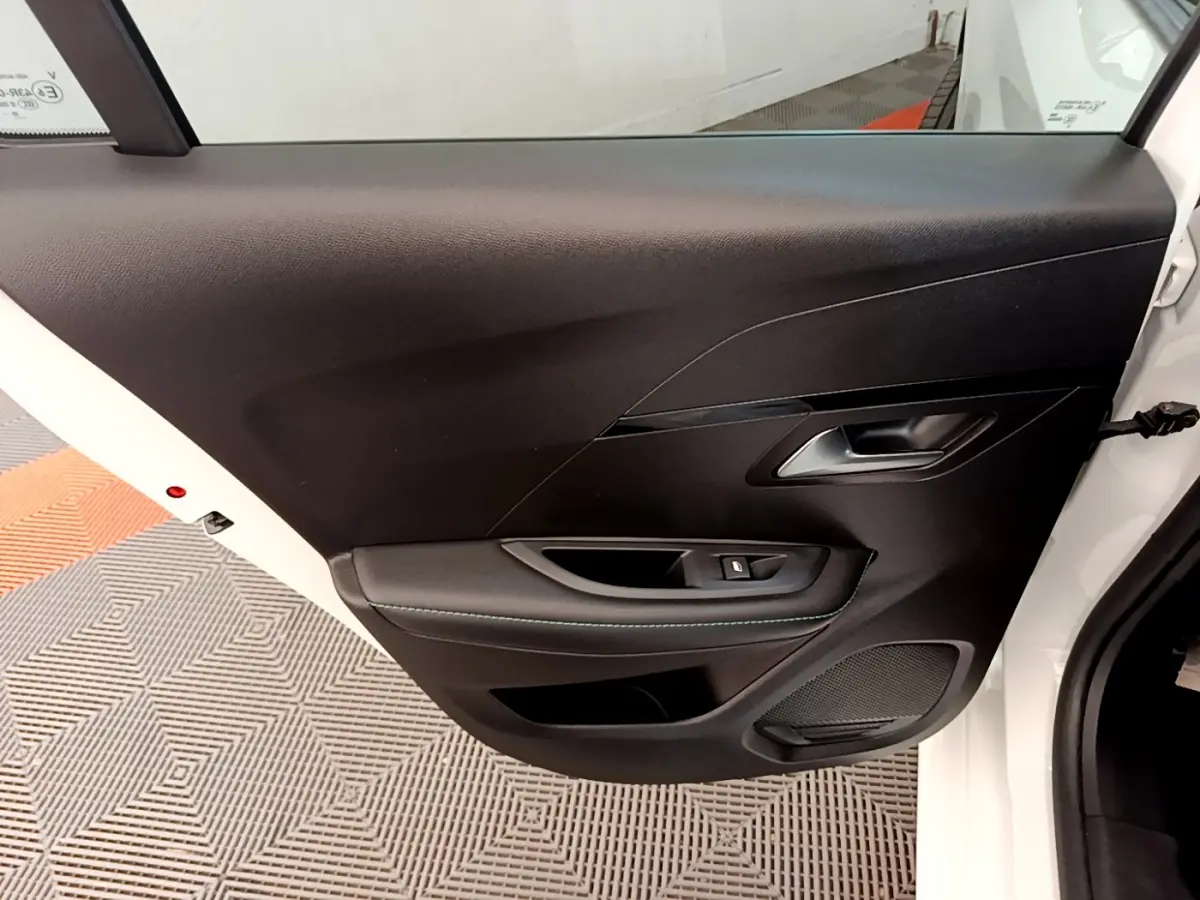 Vue rapprochée de la porte arrière droite noire avec poignée et bouton de lève-vitre d’une Peugeot 208 blanche.