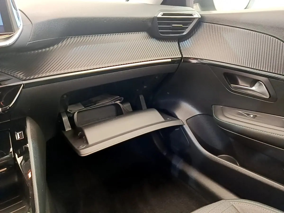 Vue intérieure côté passager du tableau de bord noir et boîte à gants ouverte de la Peugeot 208 PureTech 100 blanche.