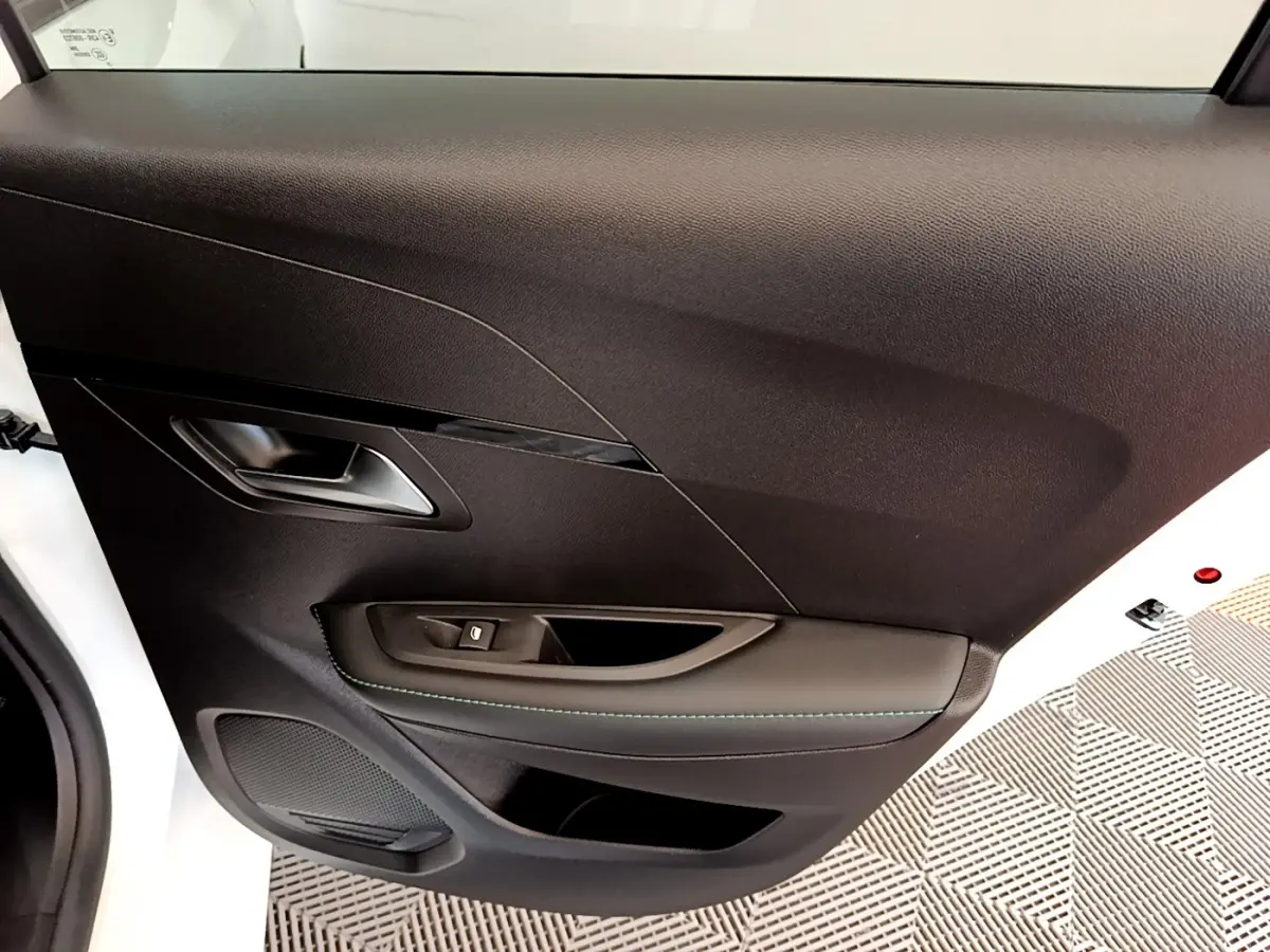 Détail de la porte intérieure côté gauche d’une Peugeot 208 blanche, avec poignée argentée et commande de vitre.