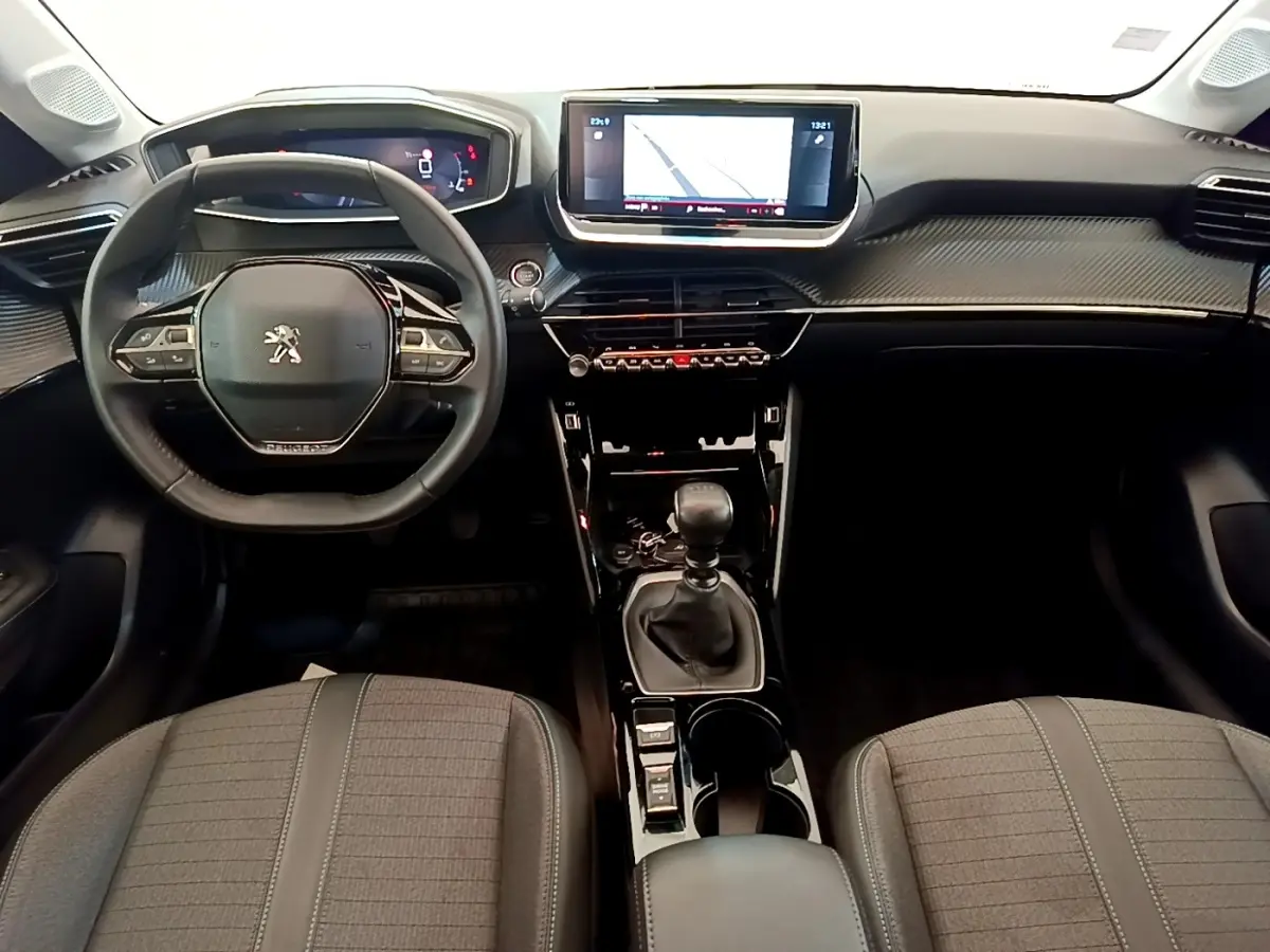 Vue intérieure frontale de la Peugeot 208 blanche, volant cuir, écran tactile 10 pouces et levier de vitesse manuel.