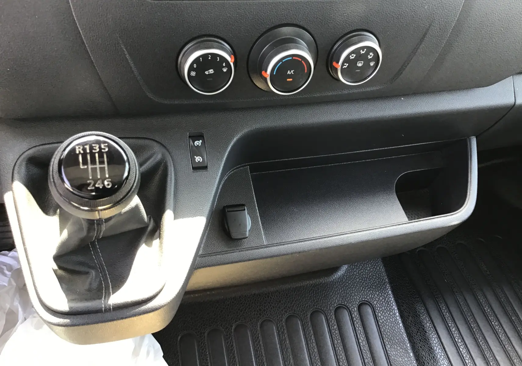 Gros plan sur la console centrale noire du Renault Master 2024, montrant le levier de vitesse manuel et les commandes de climatisation.