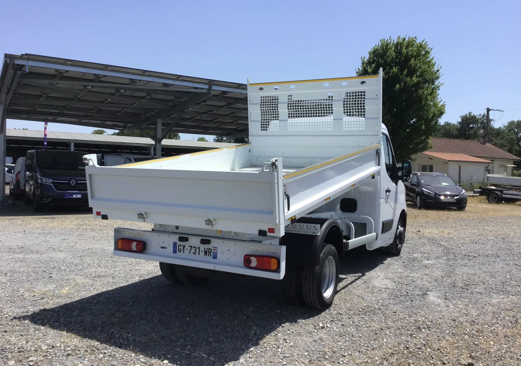 Vue 3/4 arrière droite du Renault Master blanc avec benne basculante et roues jumelées sur terrain extérieur.