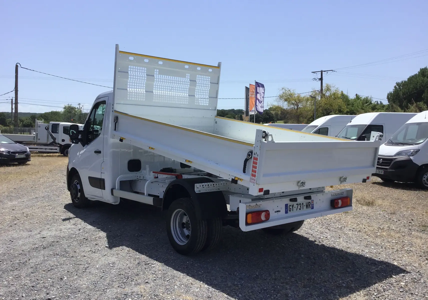 Vue 3/4 arrière droite d’un Renault Master Châssis Cabine blanc avec benne basculante et roues jumelées, stationné en extérieur.