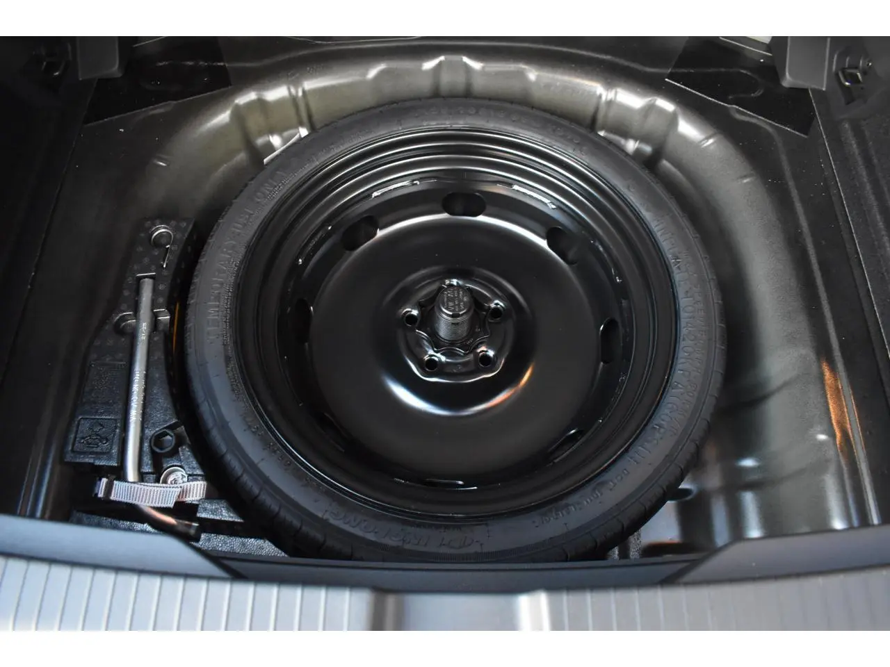 Gros plan sur la roue de secours à encombrement réduit noire dans le coffre du Volkswagen T-Roc 2025.