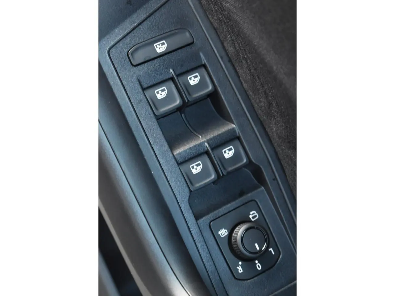 Gros plan sur les commandes de lève-vitres et réglage des rétroviseurs côté conducteur du Volkswagen T-Roc noir.