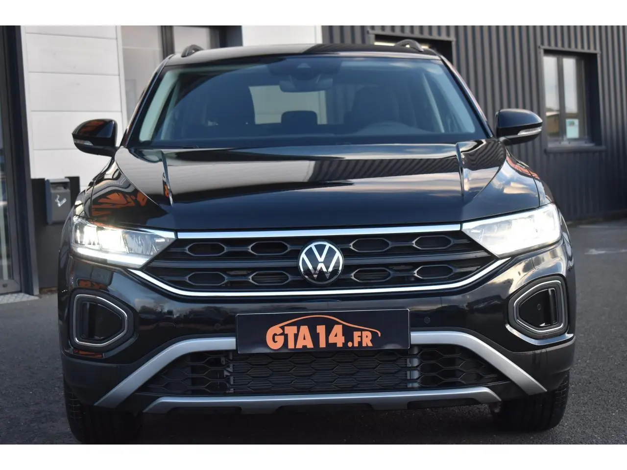 Vue frontale du Volkswagen T-Roc 2025 noir grenadilla avec phares LED allumés et calandre hexagonale distinctive.