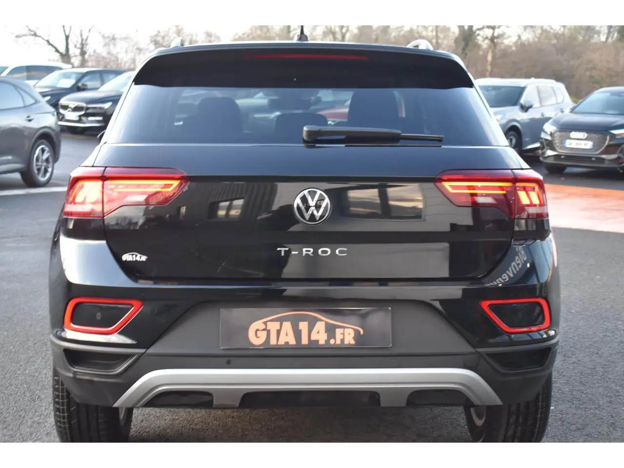 Vue arrière d'un Volkswagen T-Roc noir Grenadilla Metallic avec feux LED et détails rouges sur le pare-chocs.