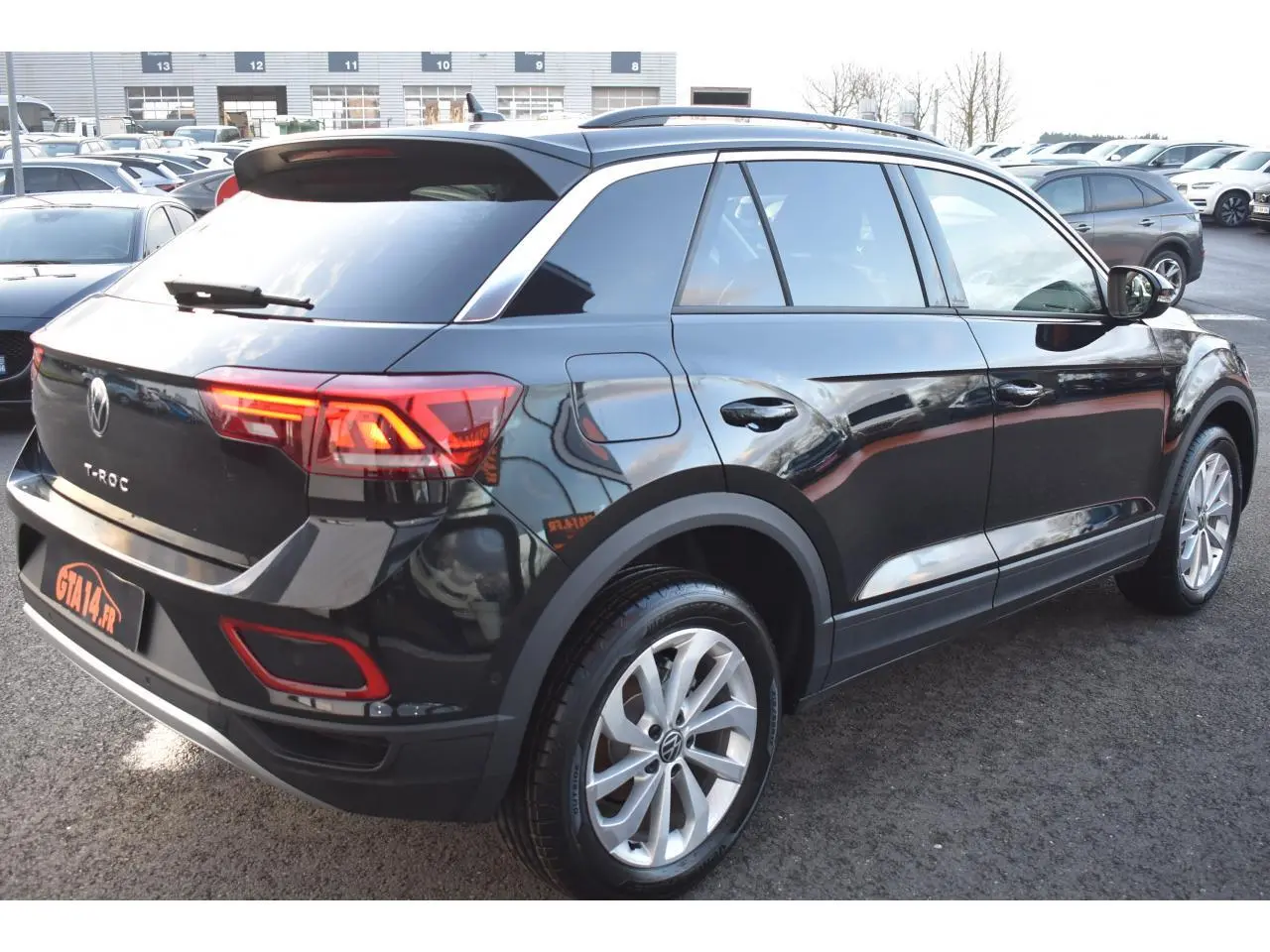 Vue 3/4 arrière droite du Volkswagen T-Roc noir métallisé avec jantes alliage 17 pouces et feux arrière LED allumés.