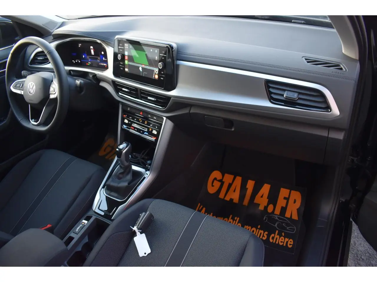 Intérieur avant droit du Volkswagen T-Roc 2025 avec sellerie noire, tableau de bord moderne et écran tactile central.