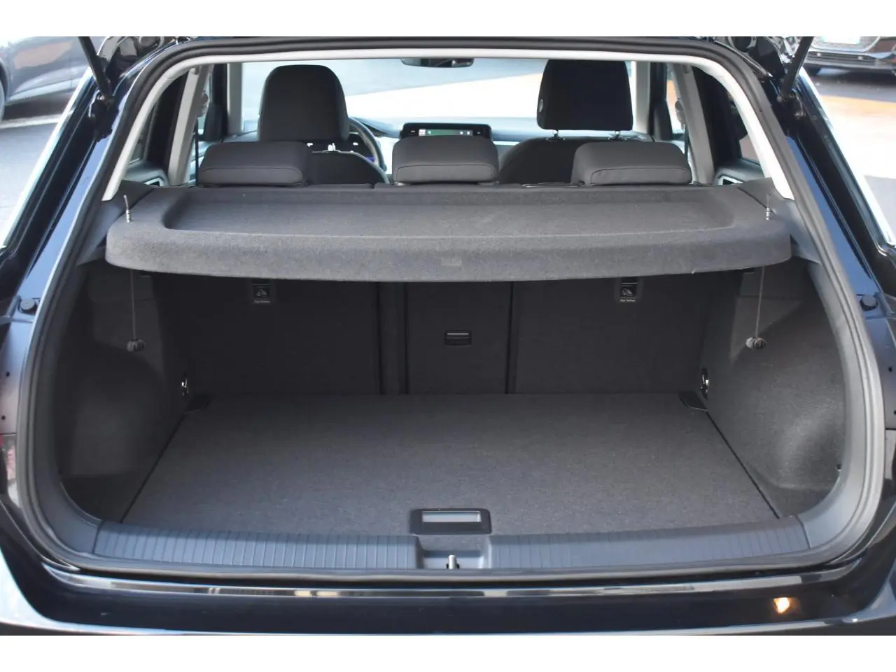 Coffre ouvert vu de l'arrière d'un Volkswagen T-Roc 2025 noir Grenadilla, avec cache-bagages et sièges arrière visibles.