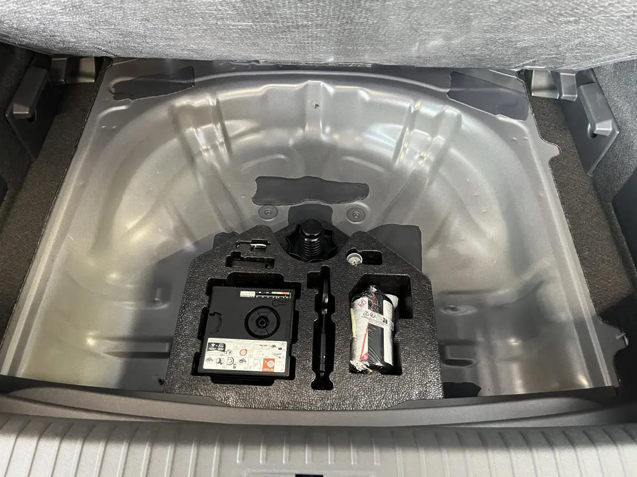 Coffre ouvert en vue plongeante du Cupra Formentor gris clair, montrant le rangement sous plancher avec kit de réparation pneus.