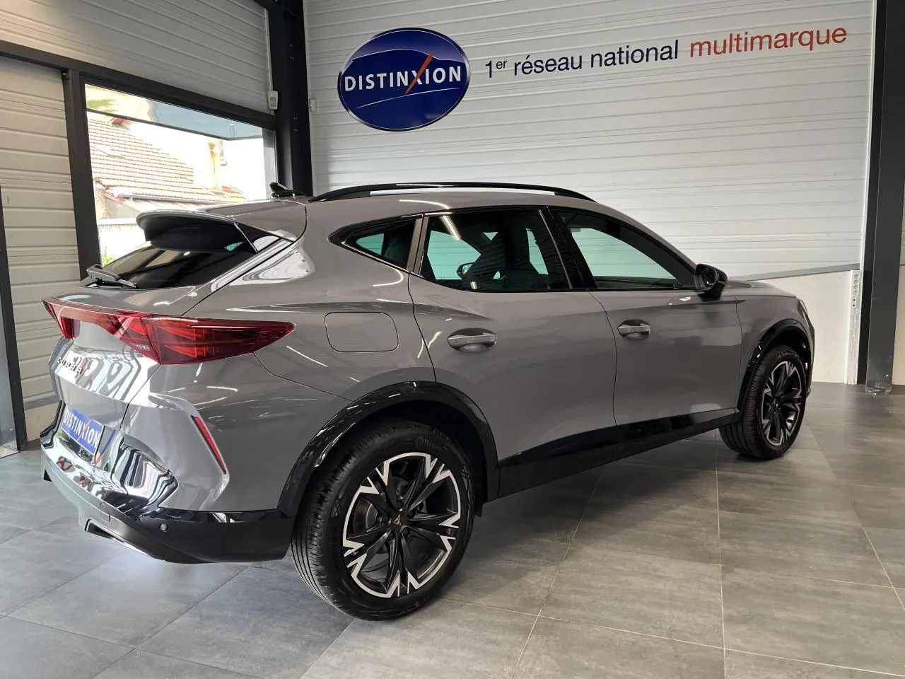 Vue 3/4 arrière droite du CUPRA Formentor gris clair avec jantes alliage 18'' et toit ouvrant panoramique en showroom.