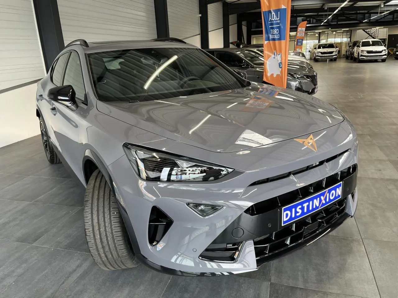 Vue 3/4 avant d'une CUPRA Formentor gris clair avec logo cuivré et calandre noire brillante en showroom.