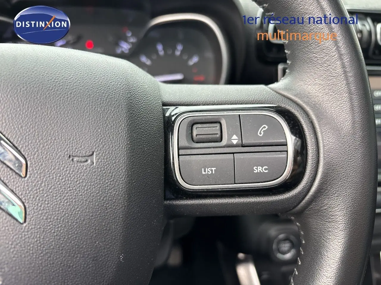 Gros plan sur les commandes à droite du volant en cuir noir du Citroën C3 Aircross Shine Gris Platinium, tableau de bord flou en arrière-plan.