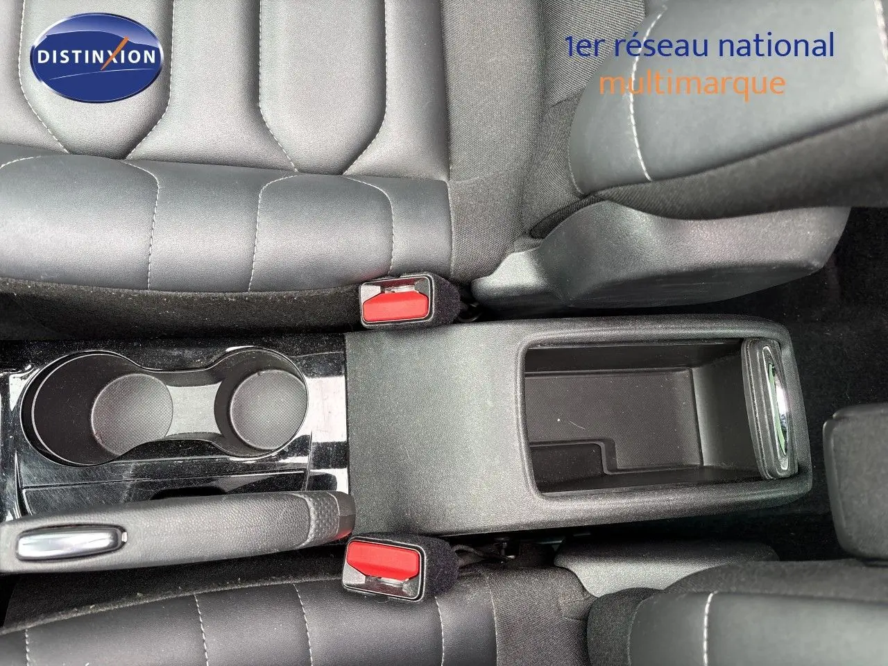 Vue plongeante sur la console centrale noire avec porte-gobelets et accoudoir entre les sièges avant en cuir noir.