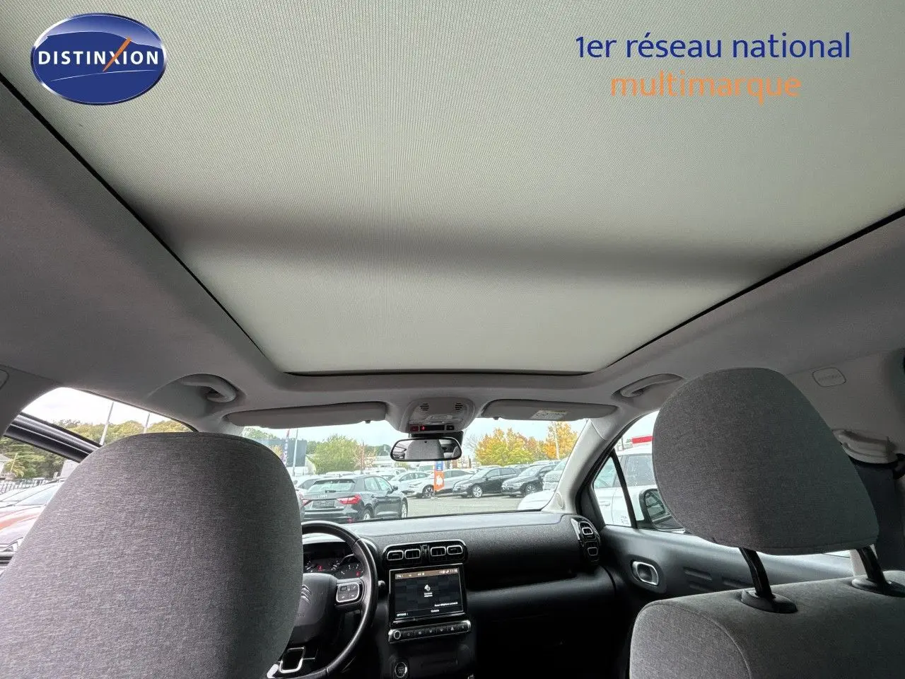 Vue intérieure avant du Citroën C3 Aircross gris, montrant le tableau de bord et le grand toit panoramique.