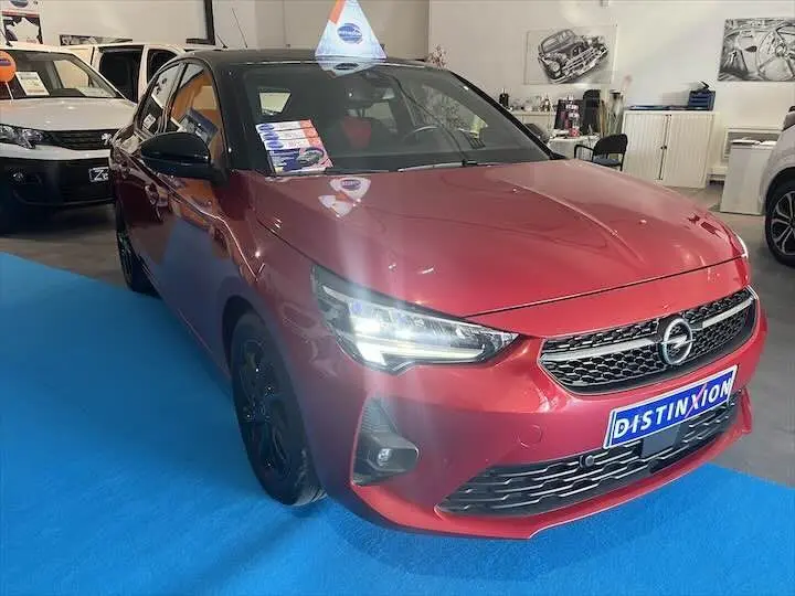Opel Corsa rouge Kardio vue 3/4 avant droit en showroom avec phares allumés et plaque Distinxion.