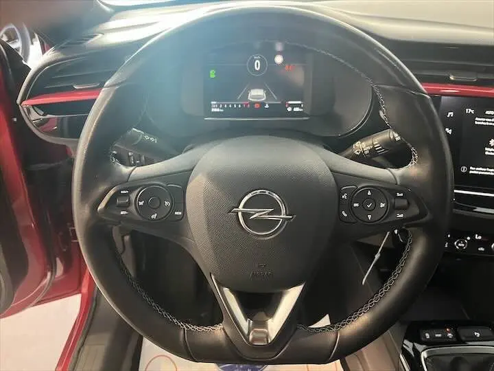 Vue rapprochée du volant noir de l'Opel Corsa rouge Kardio, avec commandes intégrées et tableau de bord numérique.
