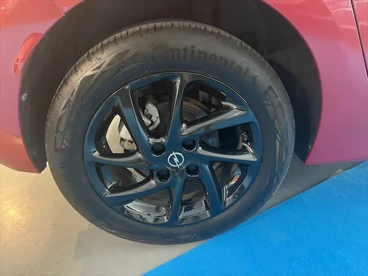 Gros plan sur la roue avant droite noire brillante d'une Opel Corsa rouge Kardio, soulignant la jante en alliage moderne.