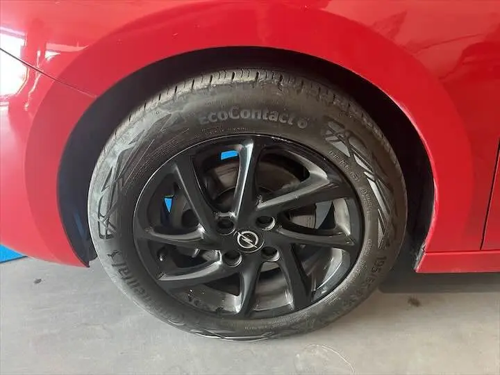 Gros plan sur la roue arrière droite d’une Opel Corsa rouge Kardio avec jante noire à cinq branches.