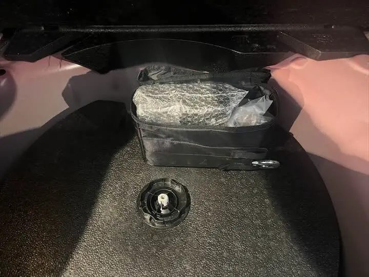 Coffre de l'Opel Corsa rouge Kardio 2021, vue intérieure montrant un rangement avec sac noir et espace de roue de secours.