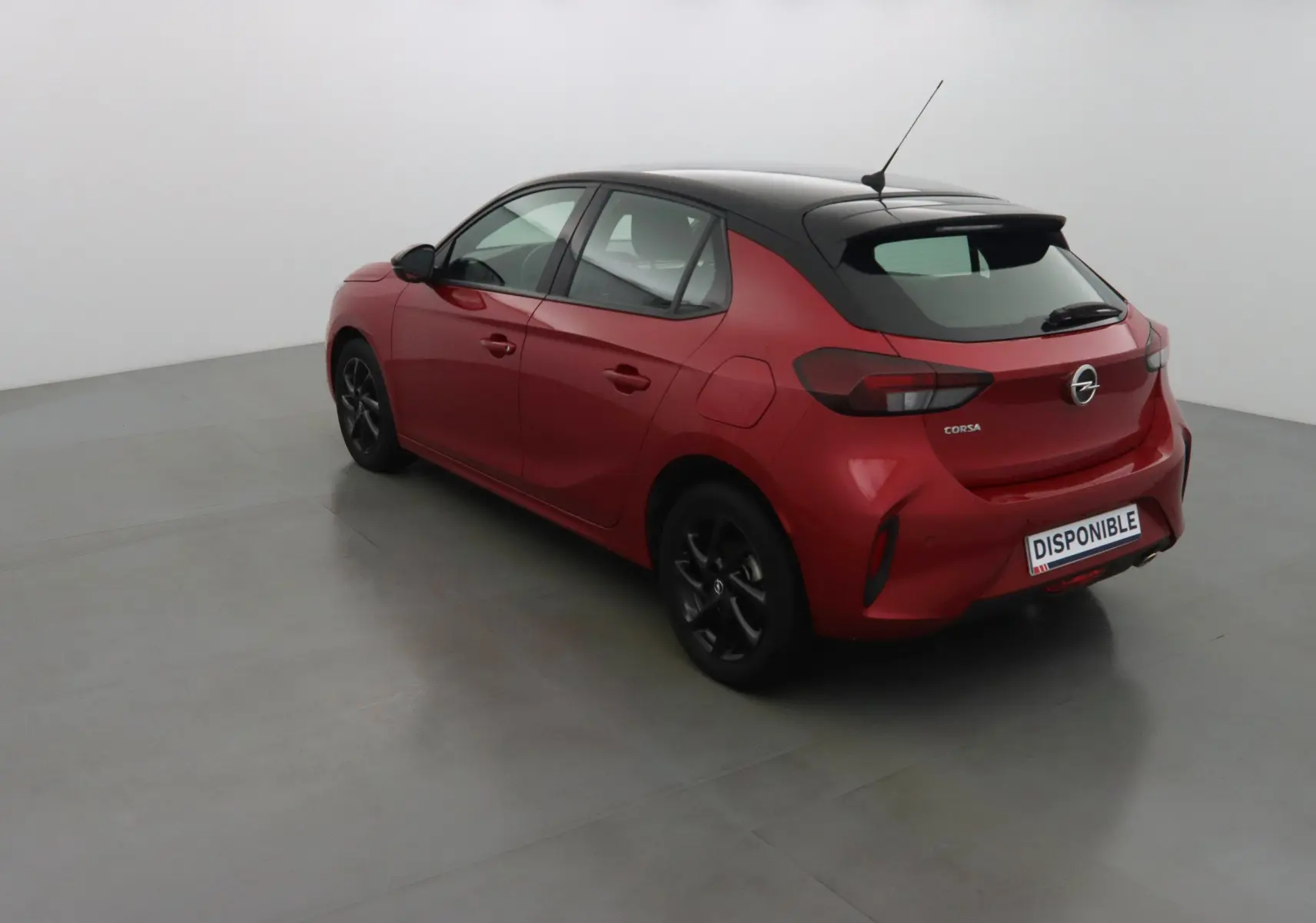 Opel Corsa rouge Kardio vue 3/4 arrière côté gauche avec toit noir et jantes noires dans un studio.