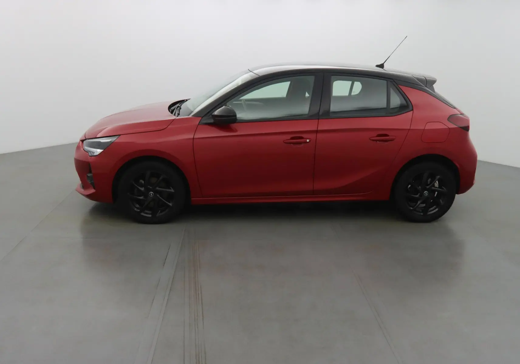 Profil côté gauche d'une Opel Corsa rouge Kardio avec jantes noires dans un studio lumineux.
