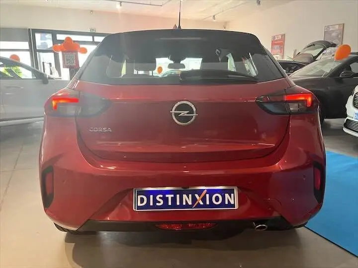 Vue arrière d'une Opel Corsa rouge Kardio avec feux allumés dans un showroom lumineux.