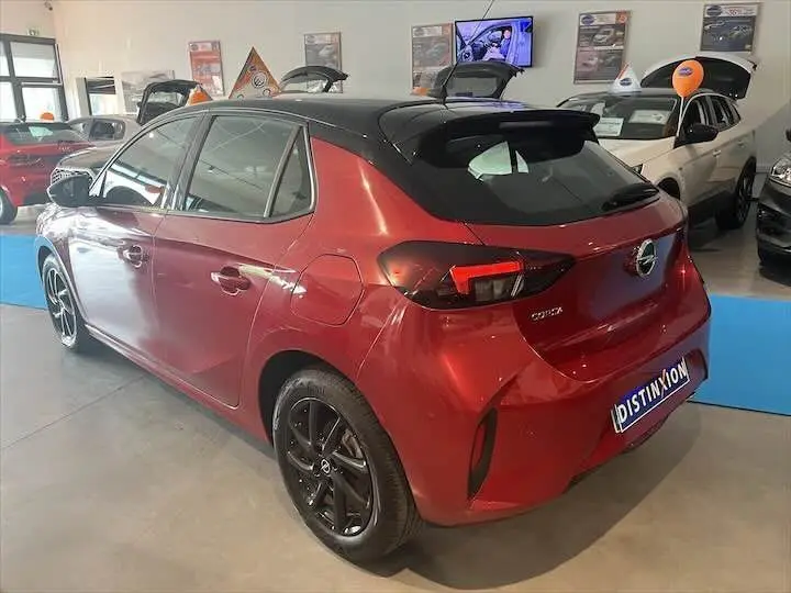 Vue 3/4 arrière droite d'une Opel Corsa rouge Kardio avec toit noir et jantes noires en showroom.