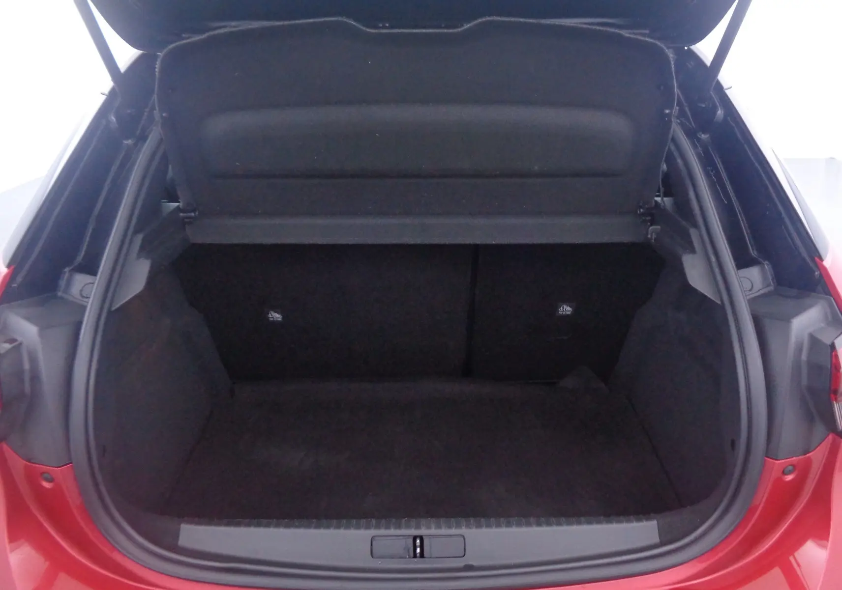 Coffre ouvert vu de l'arrière d'une Opel Corsa rouge Kardio, montrant l'espace de chargement vide et la plage arrière relevée.