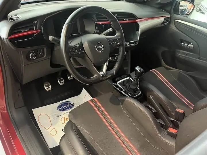 Vue intérieure côté conducteur de l'Opel Corsa rouge Kardio 2021, avec sièges noirs à bandes rouges et volant multifonction.