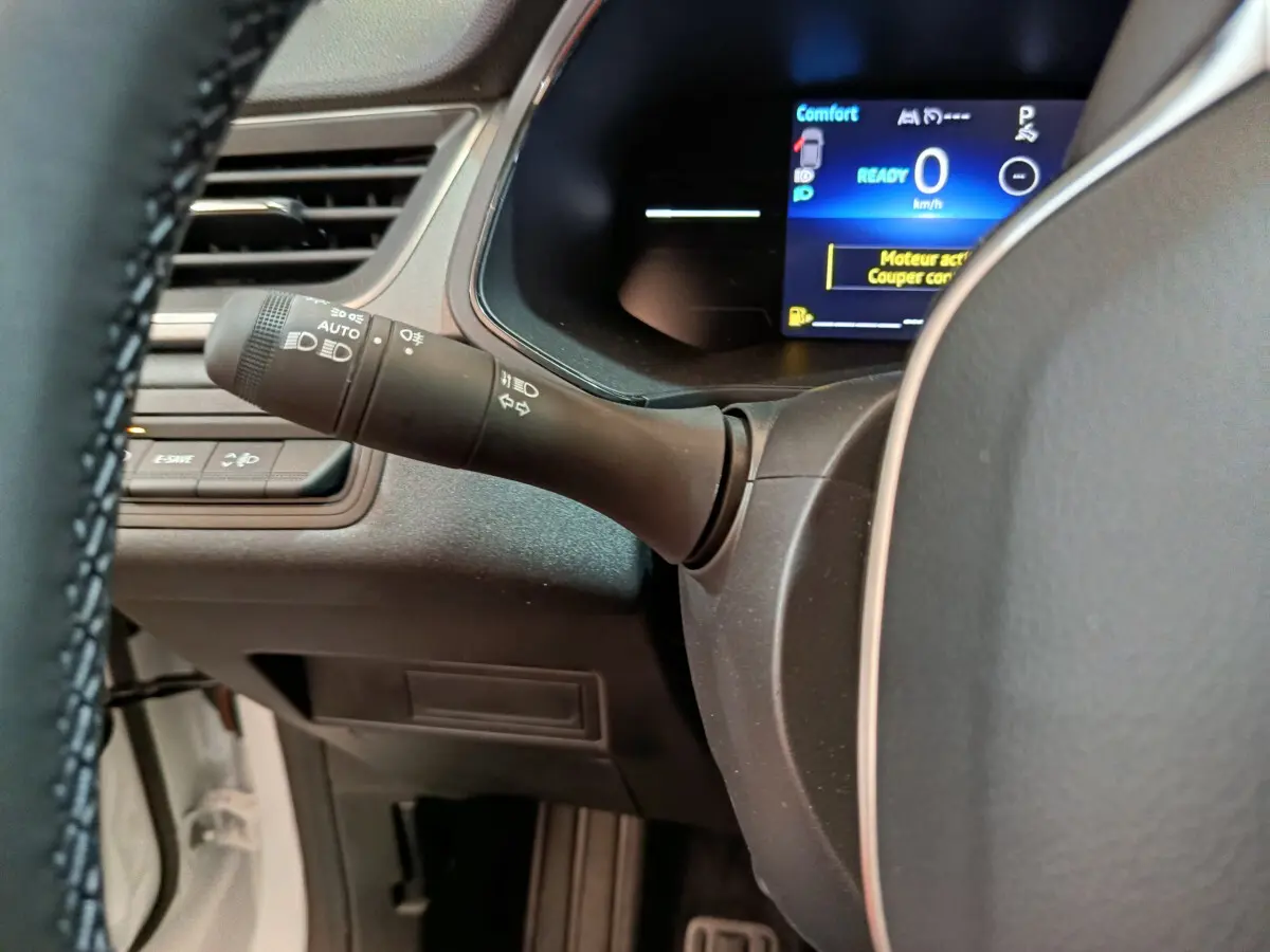 Gros plan sur la manette d'éclairage à gauche du volant cuir synthétique du Renault Captur blanc, tableau de bord numérique visible.