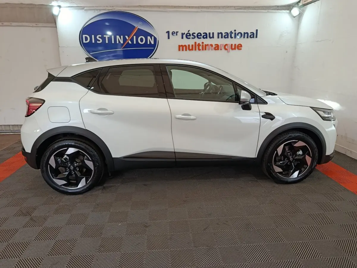 Profil côté gauche du Renault Captur blanc 2025 avec jantes noires et toit noir contrastant en intérieur showroom.