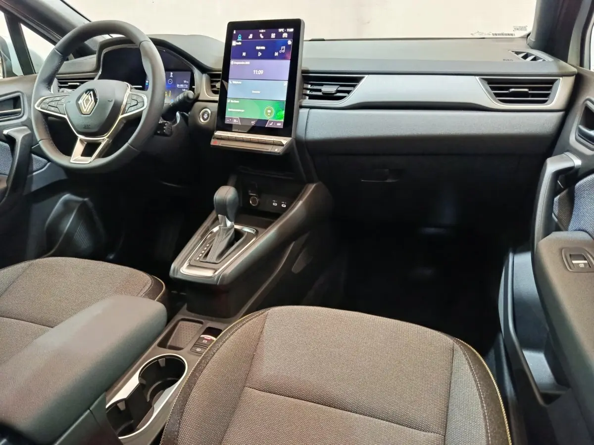 Intérieur avant du Renault Captur blanc 2025, tableau de bord moderne avec écran tactile vertical et volant multifonctions.