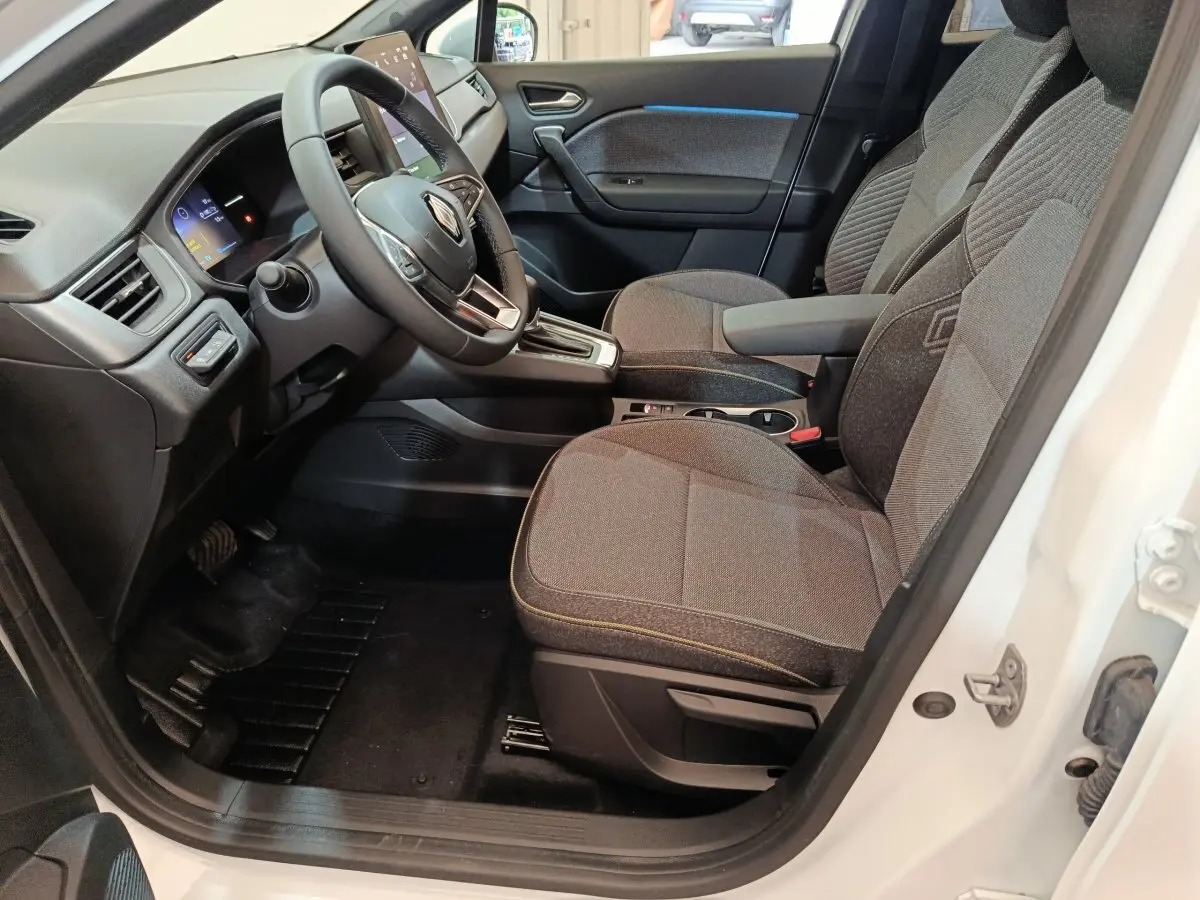 Intérieur avant droit du Renault Captur blanc 2025, sièges gris, volant multifonctions et écran tactile visible.