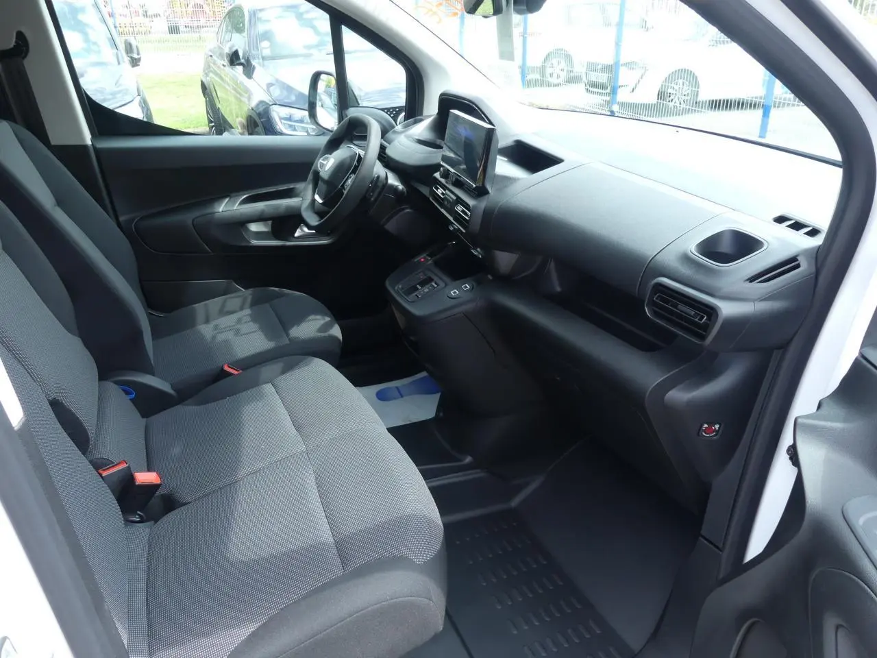 Intérieur avant droit du Peugeot Partner blanc 2025, montrant les sièges tissu et le tableau de bord moderne avec écran tactile.