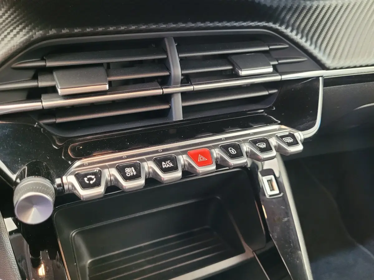 Gros plan sur la console centrale noire brillante de la Peugeot 208 2023 avec boutons de commande et aérateurs.