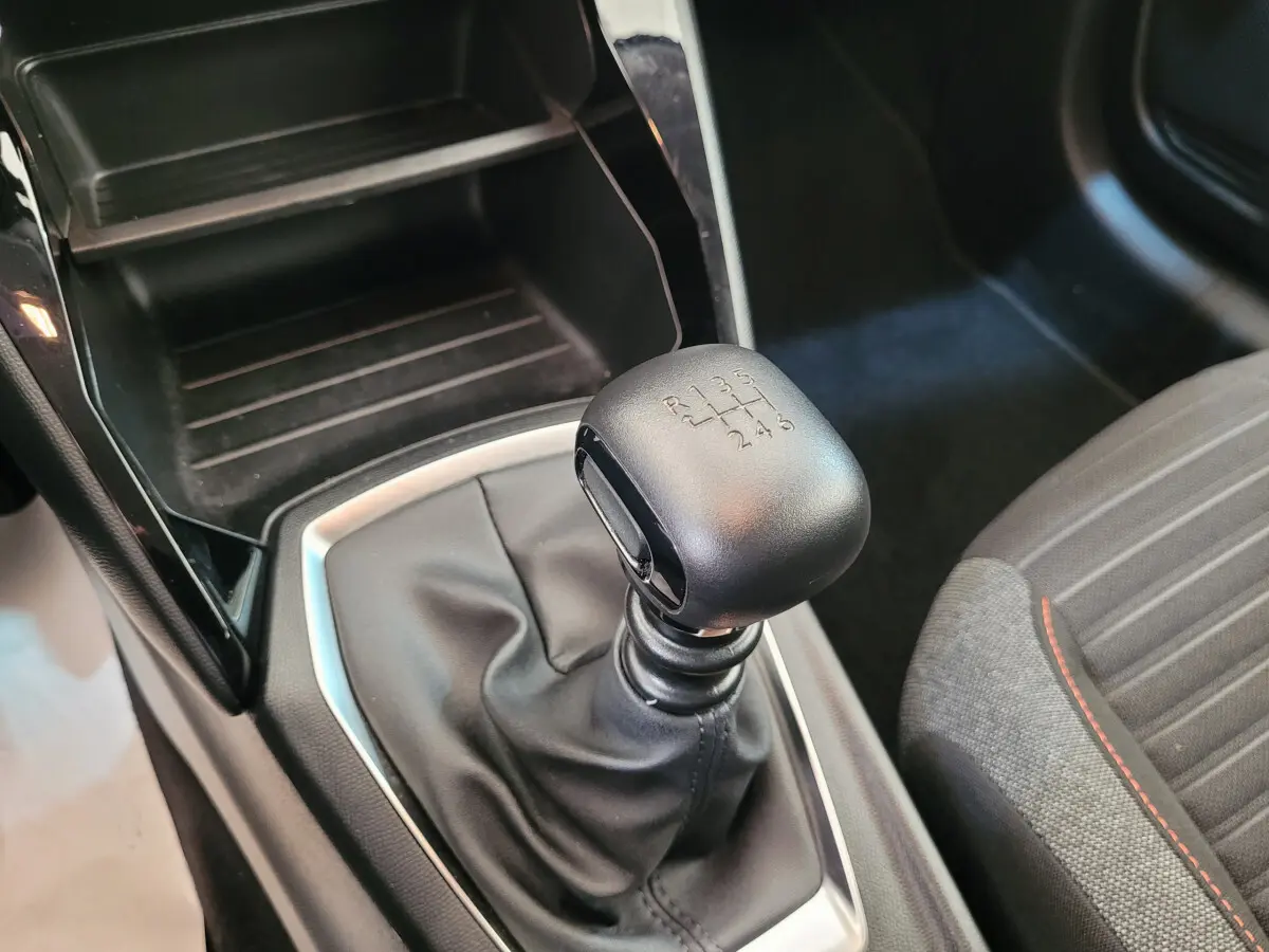 Le levier de vitesses manuel noir de la Peugeot 208 BlueHDi 100 S&S Active Pack avec coutures rouges sur siège tissu gris.