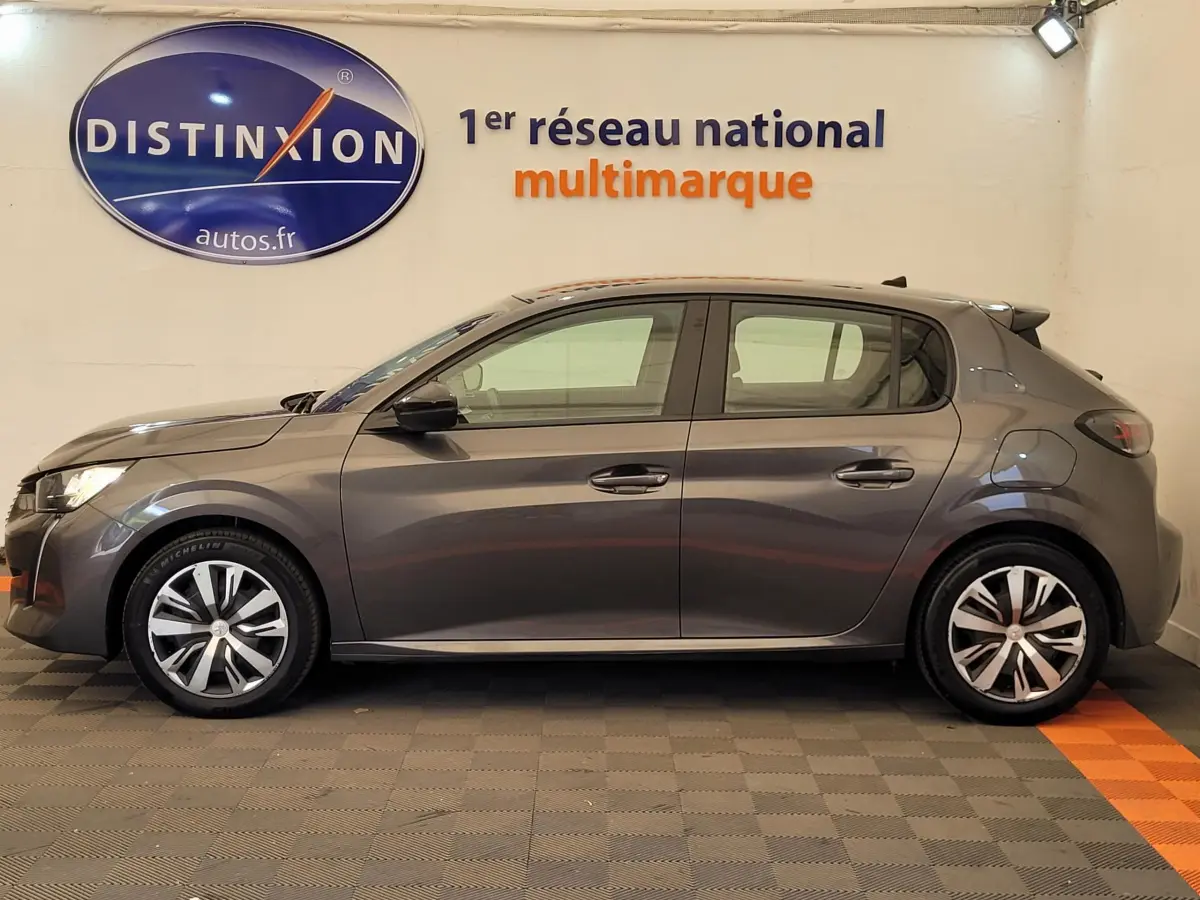 Profil côté gauche d'une Peugeot 208 BlueHDi 100 S&S Active Pack gris foncé, en intérieur sur sol carrelé.