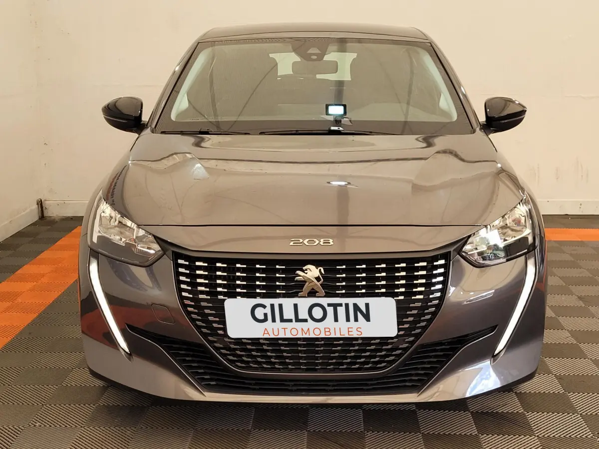 Vue frontale d'une Peugeot 208 gris foncé avec calandre noire et feux LED en forme de griffes lumineuses.