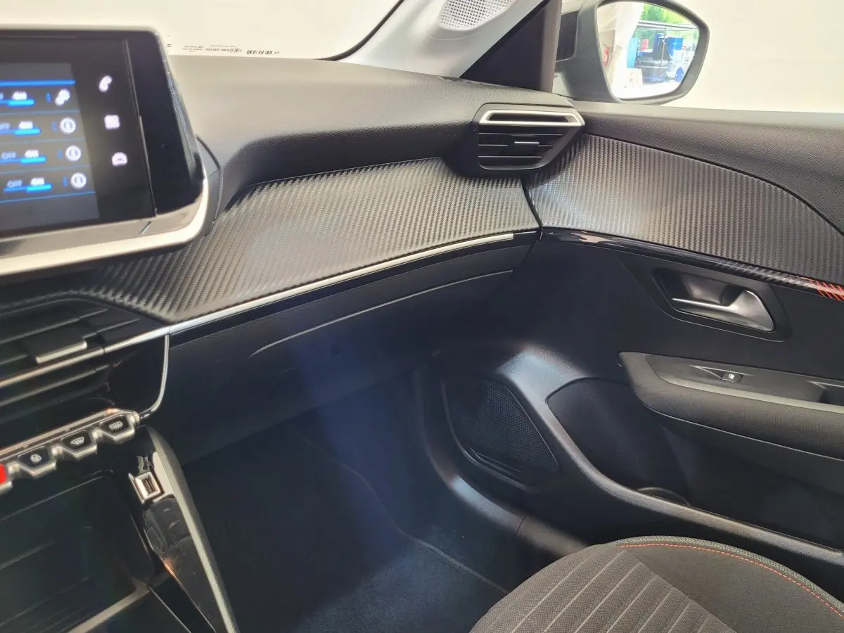 Intérieur côté passager du Peugeot 208 gris foncé 2023, tableau de bord avec finition carbone et écran tactile.