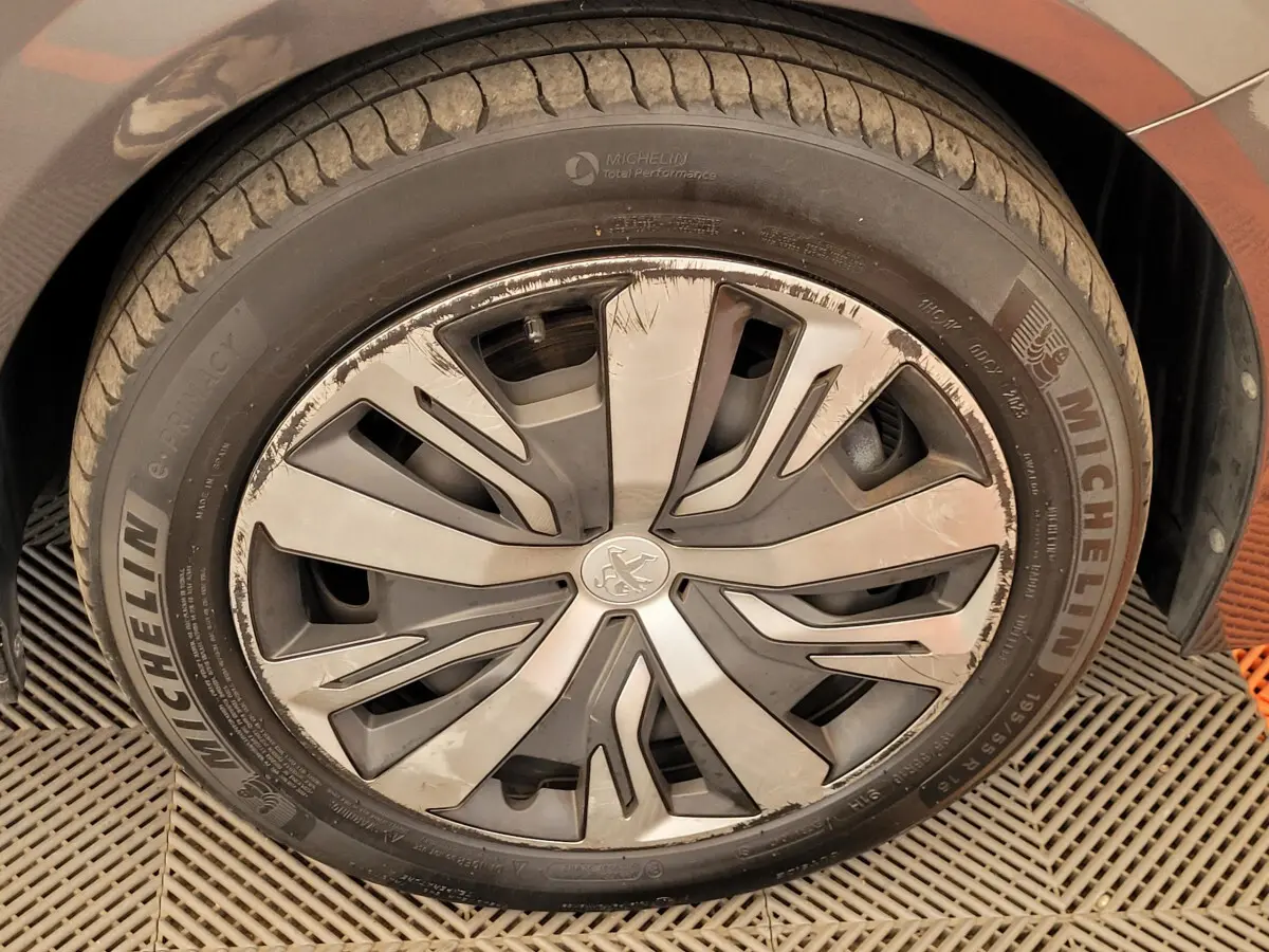 Gros plan sur la roue avant gauche d'une Peugeot 208 gris foncé avec jante alliage au design moderne et pneus Michelin.